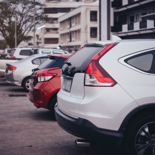 Cars parked in a lot, including a white SUV and a red hatchback