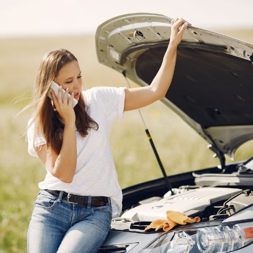 A driver on the phone beside a car with its hood open