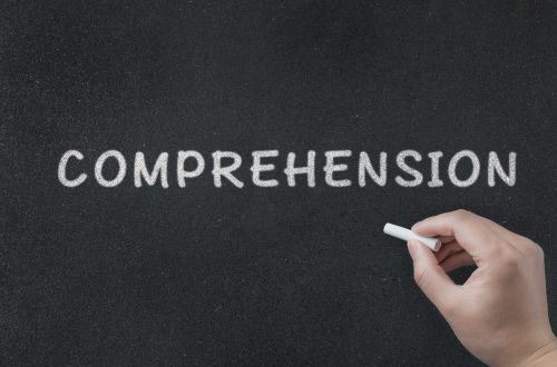 A hand writing the word comprehension on a chalkboard