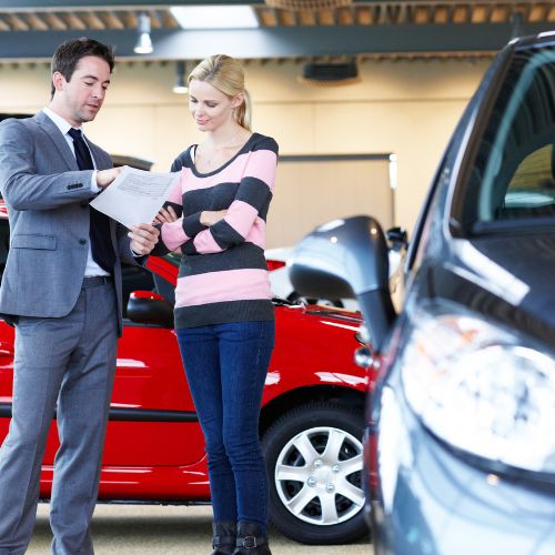 An insurance advisor going over paperwork with a customer beside a red car